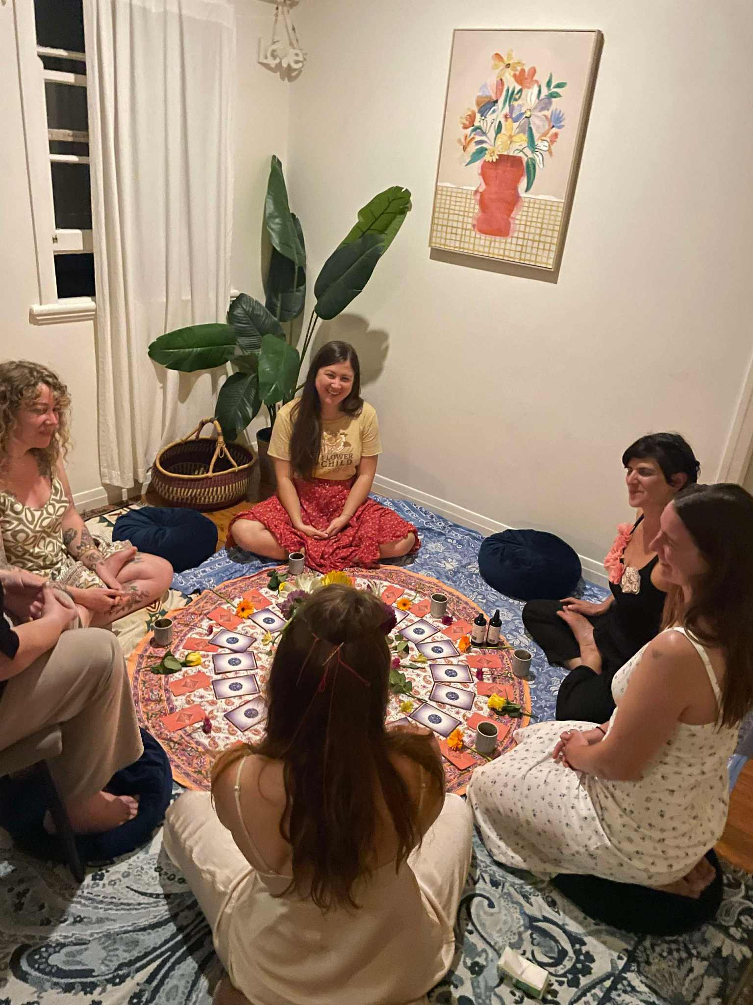 Women gathered in a circle, sitting on cushions with oracle cards spread in the center, sharing in community
